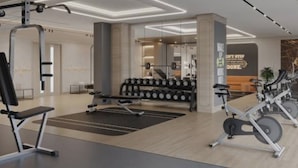 A modern gym with exercise equipment, a reception desk, and a wall with motivational text. - Nasma Holiday Homes - Azizi Riviera 46 (Dubai)