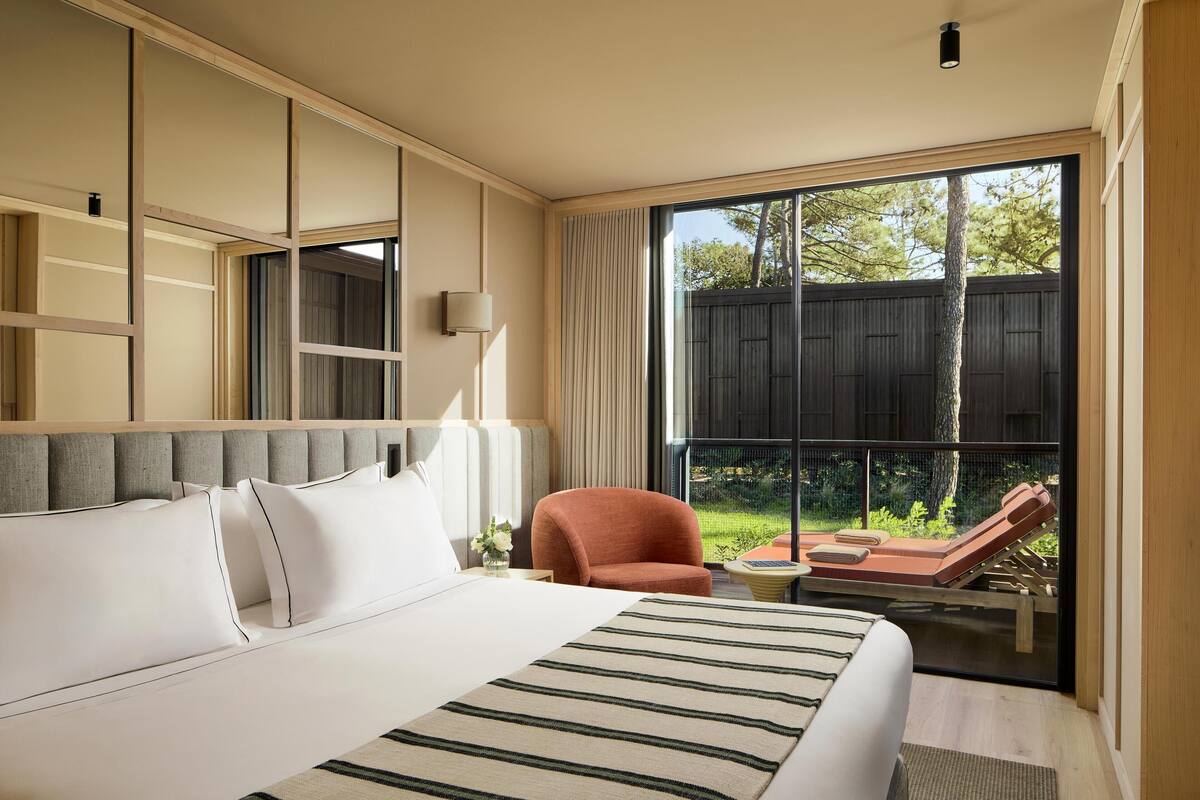 Une chambre d’hôtel avec un grand lit, une chaise, une petite table et un balcon donnant sur l’extérieur.
