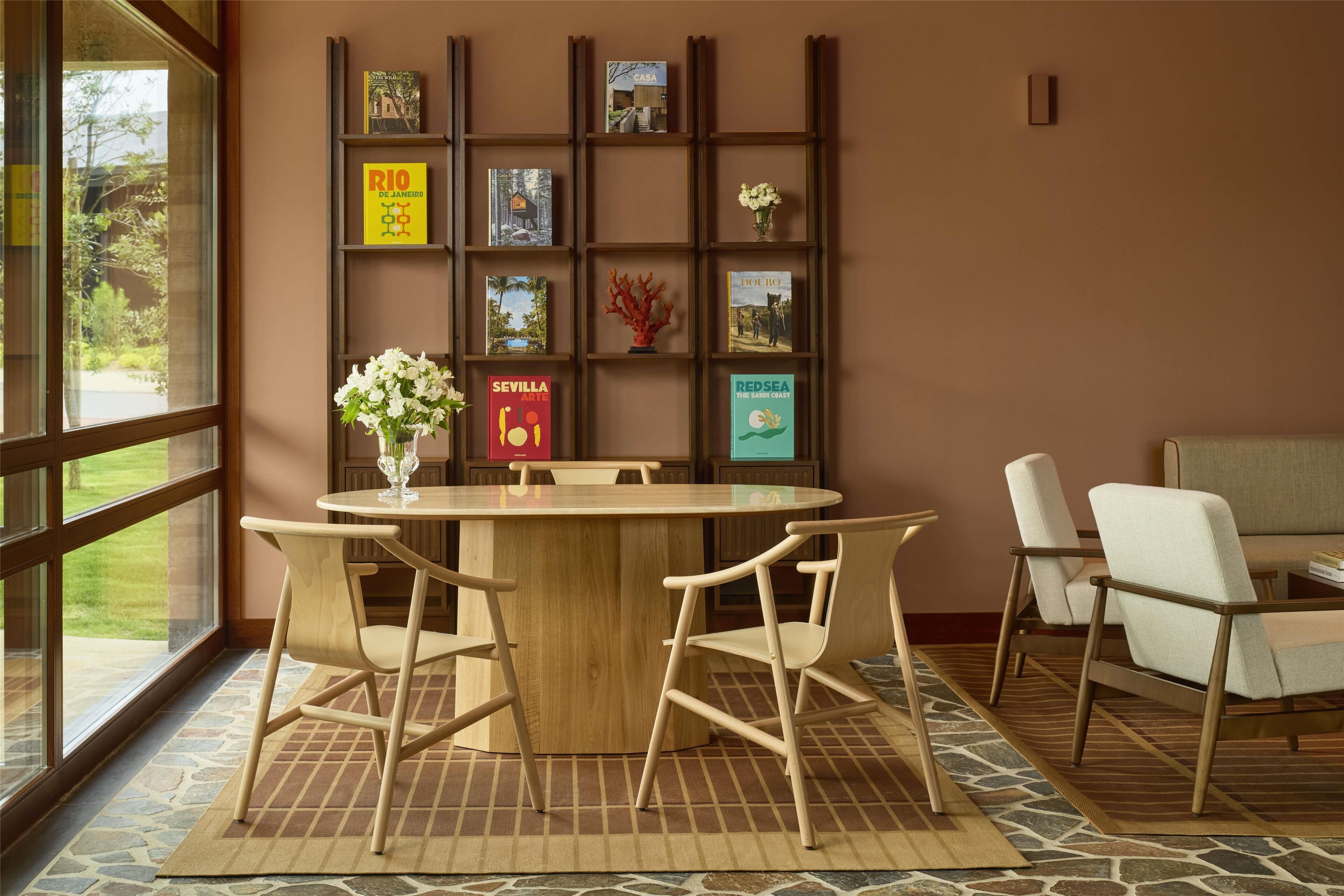 A dining area with a round table, wooden chairs, a vase with flowers, and a wall with framed pictures.