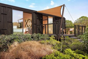 Un edificio moderno con amplios ventanales, una terraza con mobiliario exterior y diversas plantas en primer plano.