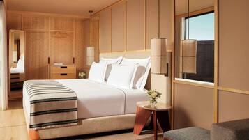Una habitación de hotel moderna con una cama grande, mesitas de noche, una pequeña mesa redonda con un jarrón de flores y vistas al exterior a través de una ventana.