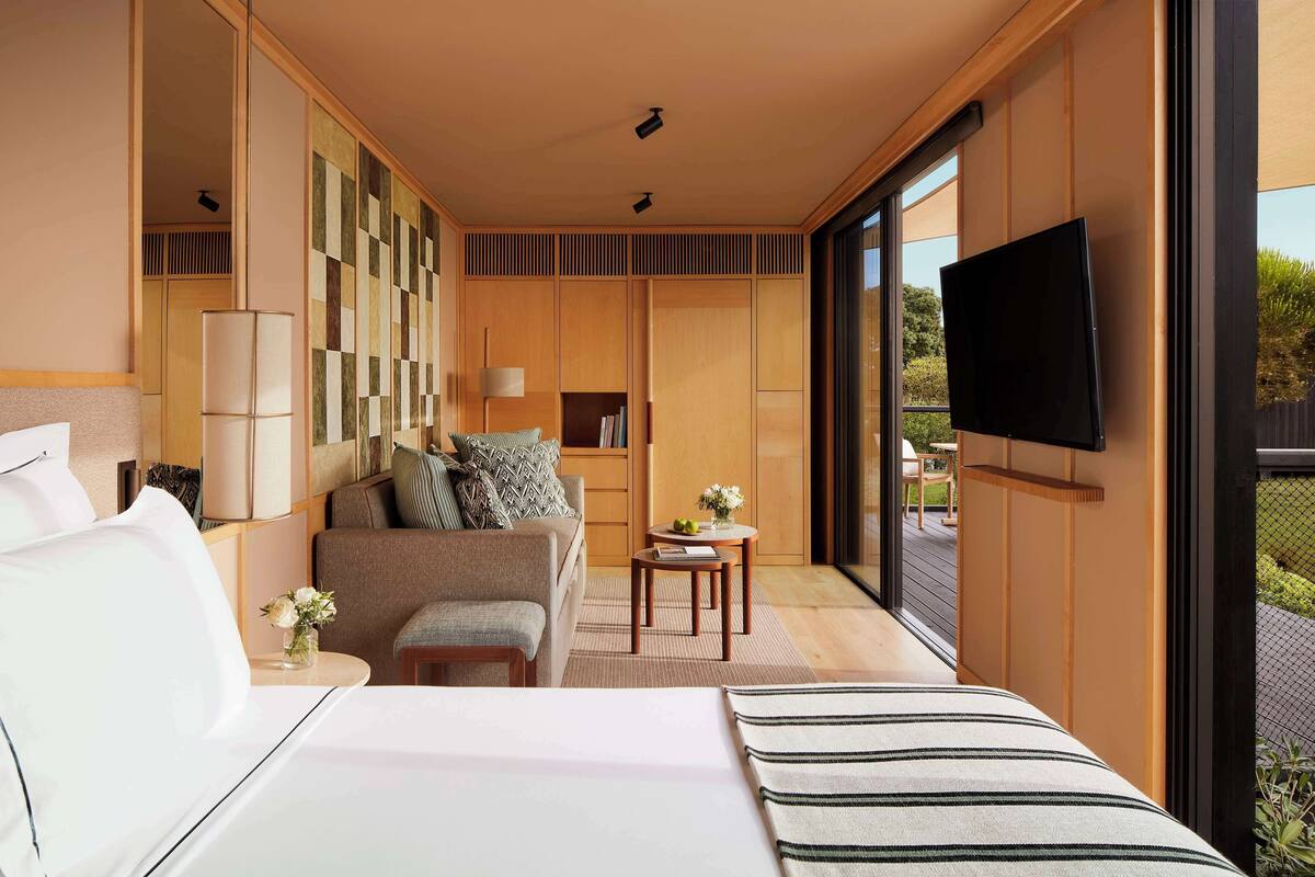 Une chambre d’hôtel moderne avec un grand lit, un canapé, une petite table avec une lampe et un téléviseur fixé au mur.
