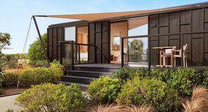Ein modernes Haus mit einer großen Glasdoor, einer Holzdielen-Terrasse und einem Essbereich mit Gartenmöbeln.