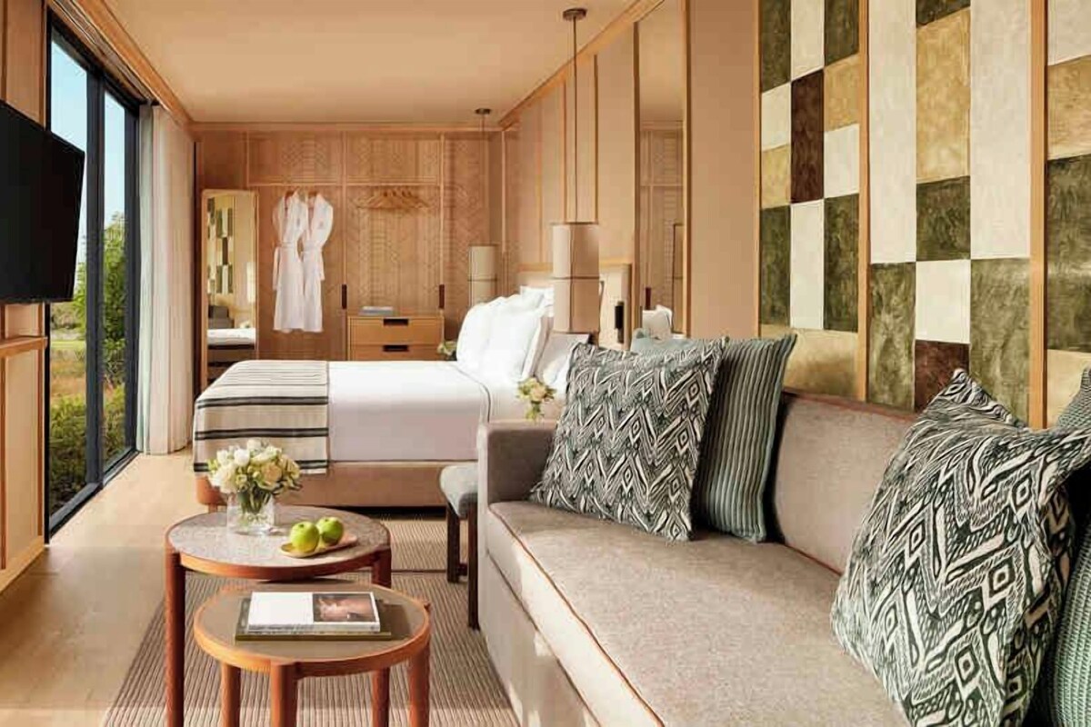 A modern hotel room with a large bed, a sofa, a TV, and a view of the outdoors.
