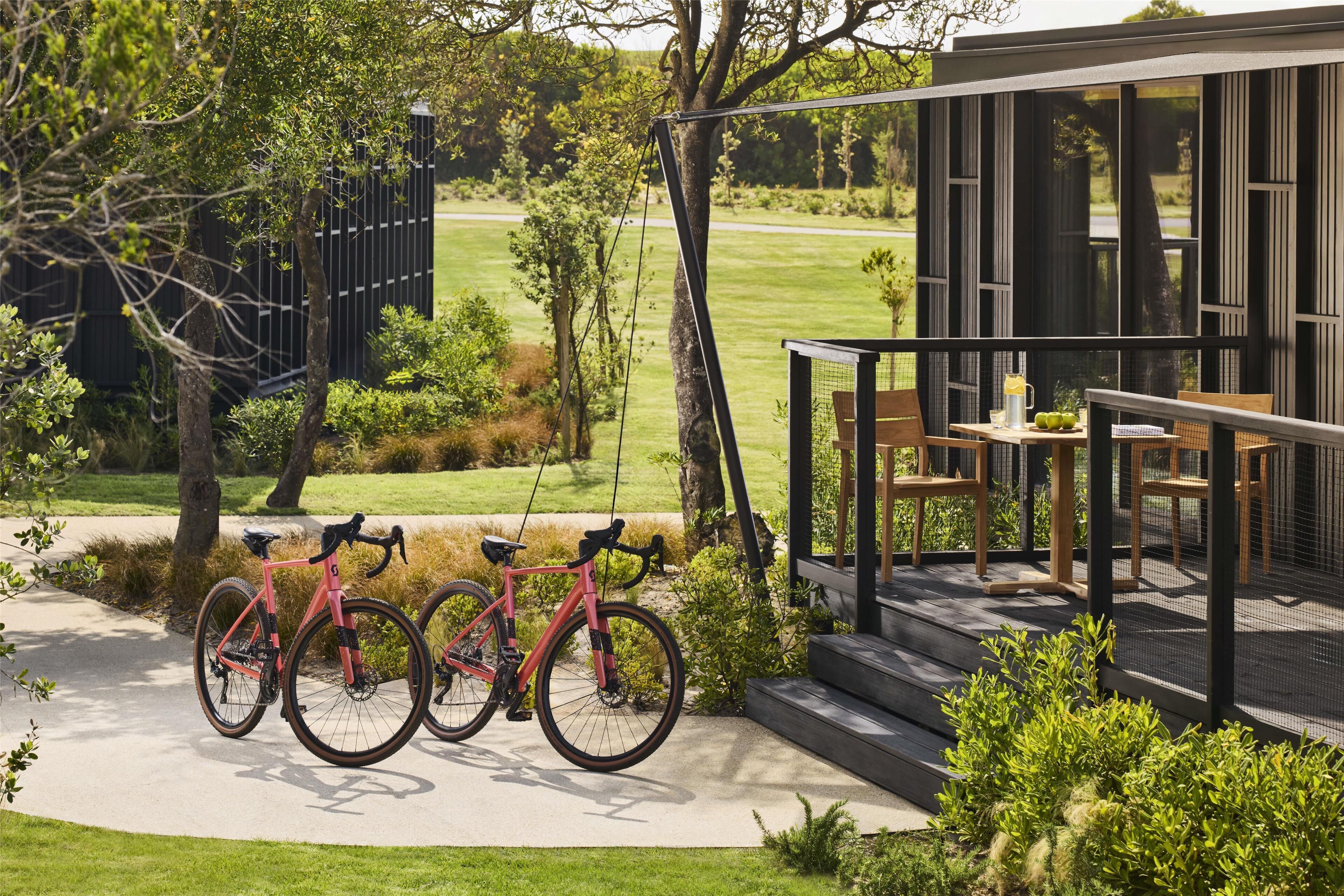 A modern outdoor seating area with a table and chairs, a bicycle parked nearby, and a view of a green landscape.