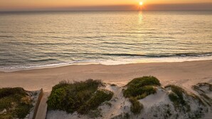 A beach with a sunset over the ocean, sandy dunes, and a path leading to the water. - Tivoli Estela Golf & Lodges Porto (Povoa De Varzim)