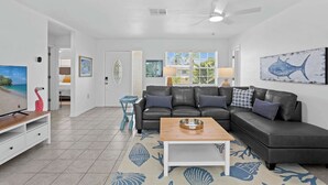 A living room with a sectional sofa, a coffee table, a TV, and a large window with a view of palm trees. - Heated Pool, Bay Views & Kayak Launch — 6 Guests (Bradenton)