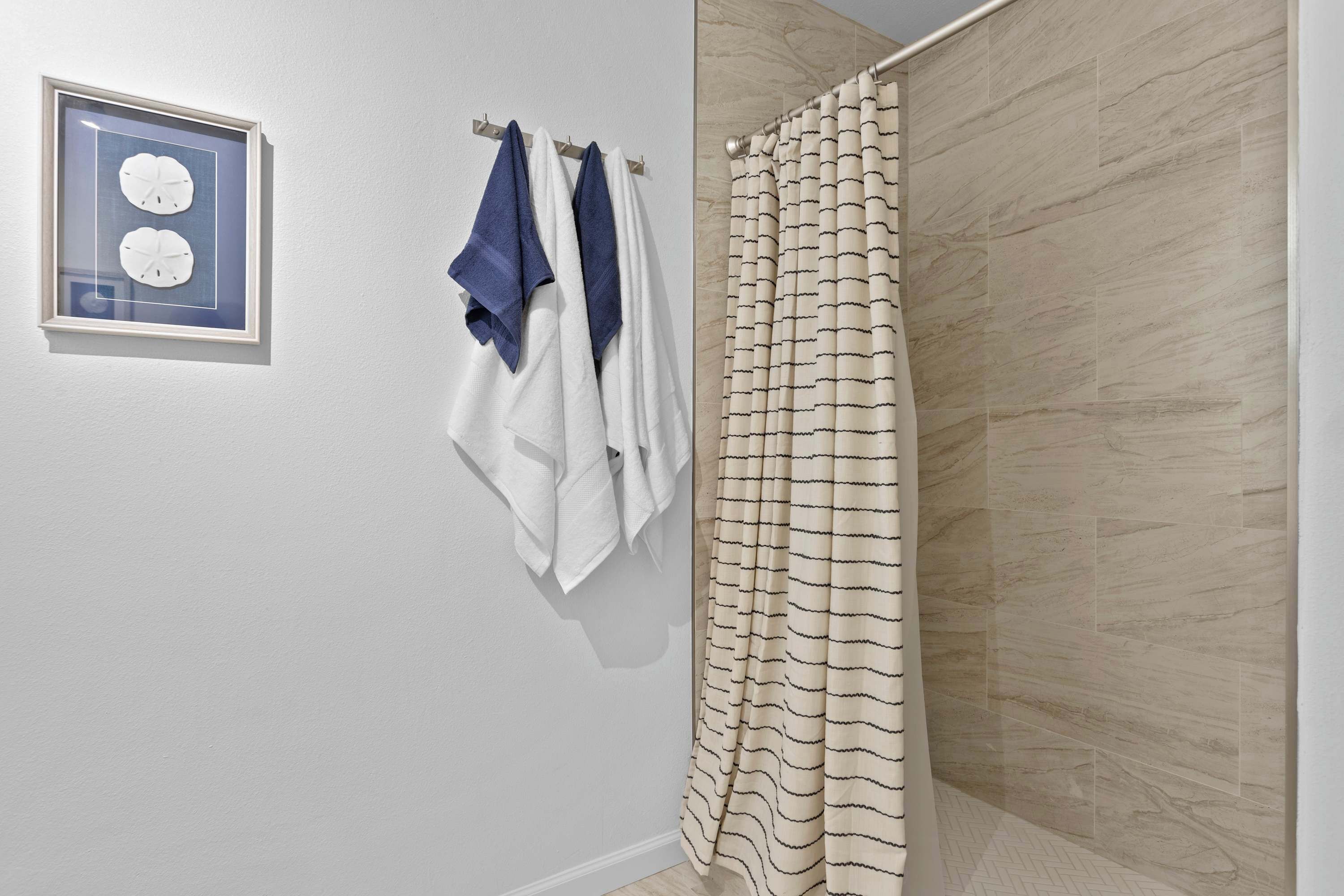 A bathroom with a shower curtain, a towel rack with towels, and a framed picture on the wall.