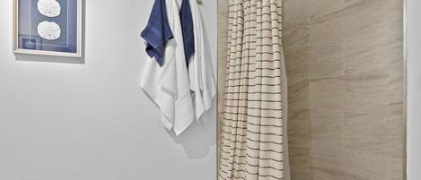 A bathroom with a shower curtain, a towel rack with towels, and a framed picture on the wall.