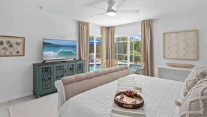 A bedroom with a bed, a TV, a ceiling fan, a window with curtains, a view of a pool, and a framed picture on the wall. - Heated Pool, Bay Views & Kayak Launch — 6 Guests (Bradenton)