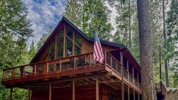 A wooden cabin with a balcony, large windows, and an American flag.