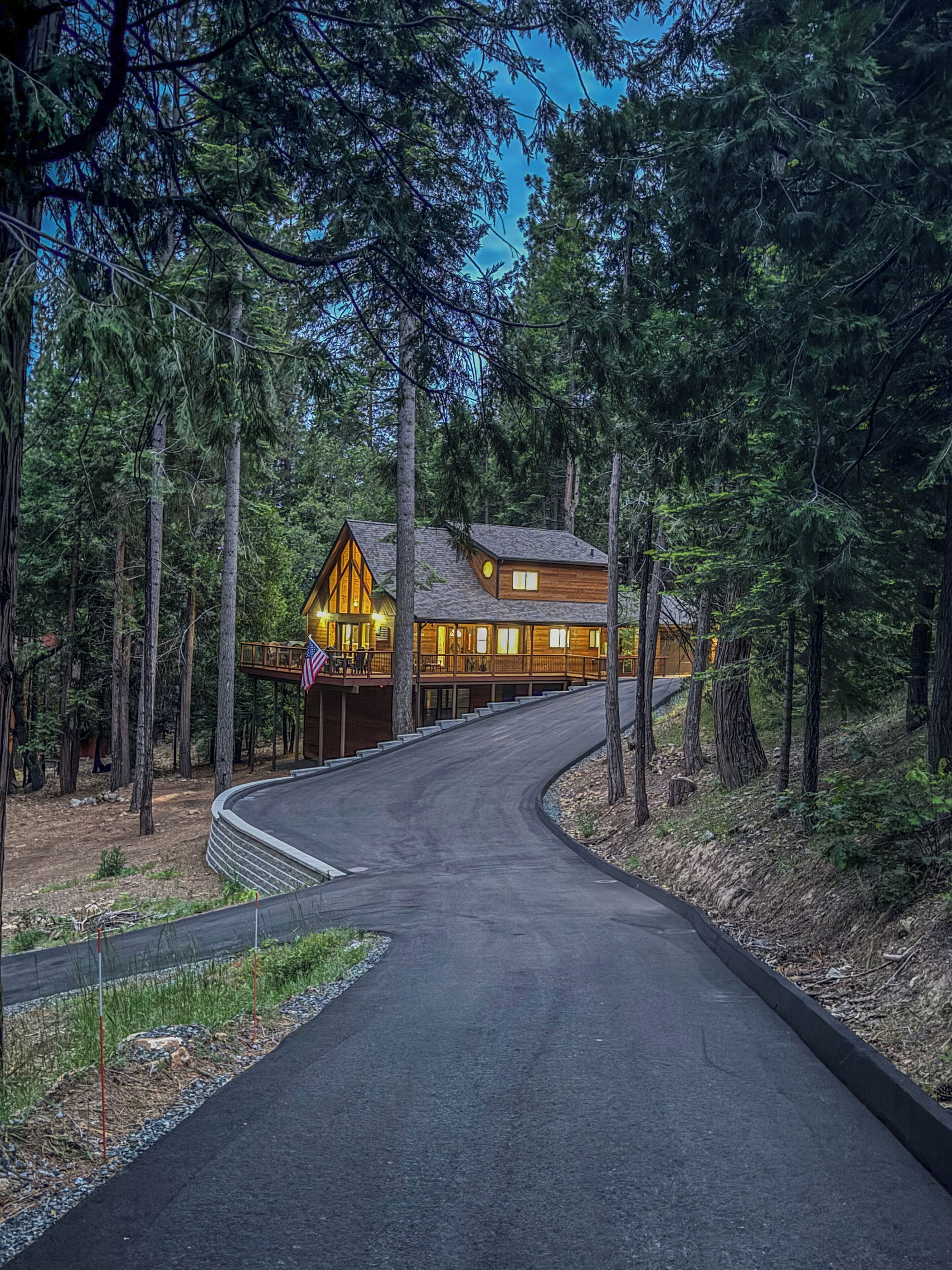 A wooden cabin with a curved driveway, surrounded by tall trees.