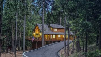 A wooden cabin with a curved driveway, surrounded by tall trees.