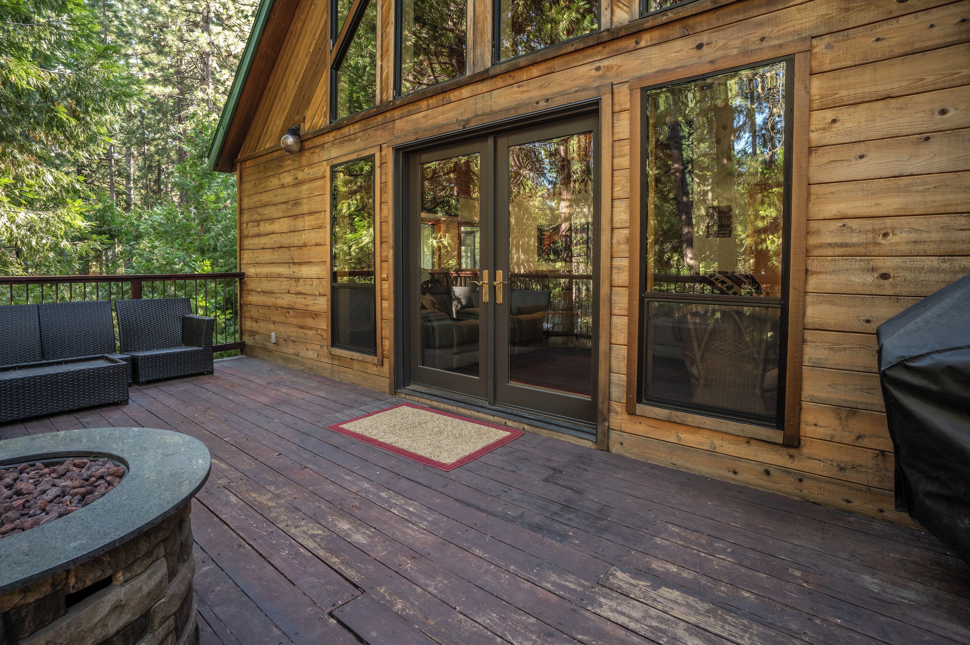 A wooden deck with outdoor furniture, a fire pit, and large sliding glass doors leading to an interior space.