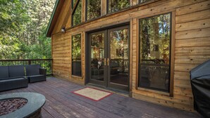 Une terrasse en bois avec des meubles d’extérieur, un foyer et de grandes portes-fenêtres coulissantes donnant sur un espace intérieur.