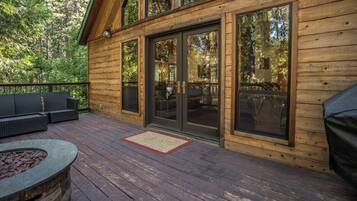 A wooden deck with outdoor furniture, a fire pit, and large sliding glass doors leading to an interior space.