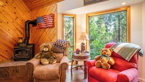 L’intérieur chaleureux d’un chalet avec une cheminée, deux fauteuils confortables et une grande fenêtre donnant sur la forêt.