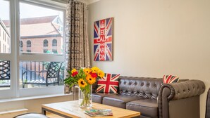 Una sala de estar con un sofá, una mesa de centro con un jarrón de flores y una ventana con cortinas.