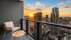 Un balcón con vistas a un paisaje urbano al atardecer, una silla y una mesa redonda pequeña.