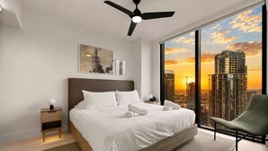 Un dormitorio moderno con una cama grande, una mesita de noche, una silla y vistas a la ciudad.