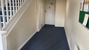 A hallway with a white staircase, a door at the end, and a bulletin board on the wall. - Spacious Tidy Room in Cardiff City (Cardiff)
