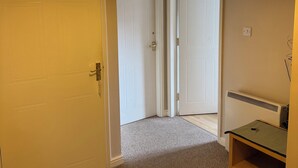 A hallway with carpeted flooring, white doors, a hanging light fixture, and a small wooden table with a key on it. - Spacious Tidy Room in Cardiff City (Cardiff)