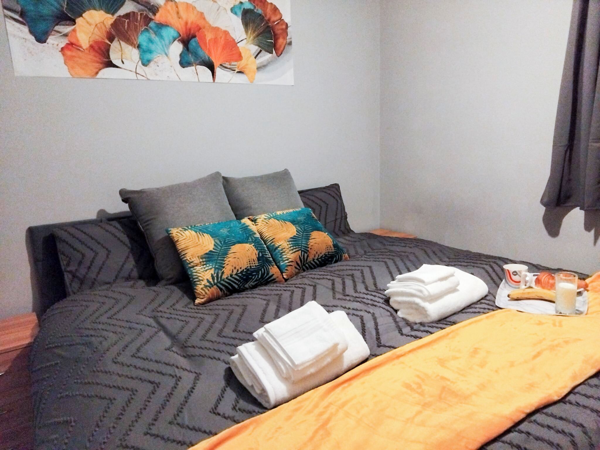 A neatly made bed with a patterned bedspread, two pillows, and a folded white towel.