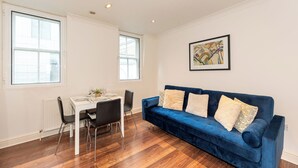 Uma sala de estar moderna com um sofá azul, uma mesa de jantar com cadeiras e janelas amplas.
