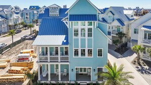 A multi-story house with a blue roof and white trim, surrounded by other similarly styled homes.
