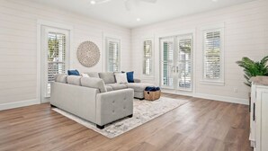 A spacious living room with a grey sectional sofa, a ceiling fan, and large windows with blinds.