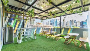 A rooftop terrace with artificial grass, wooden tables, potted plants, and a city skyline view. - Redenza Suites Makati (Makati)