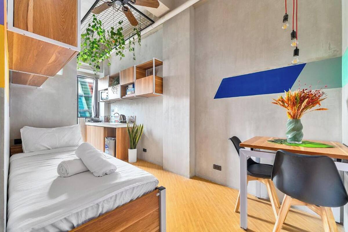 A modern hotel room with a bed, a desk, and a dining area.