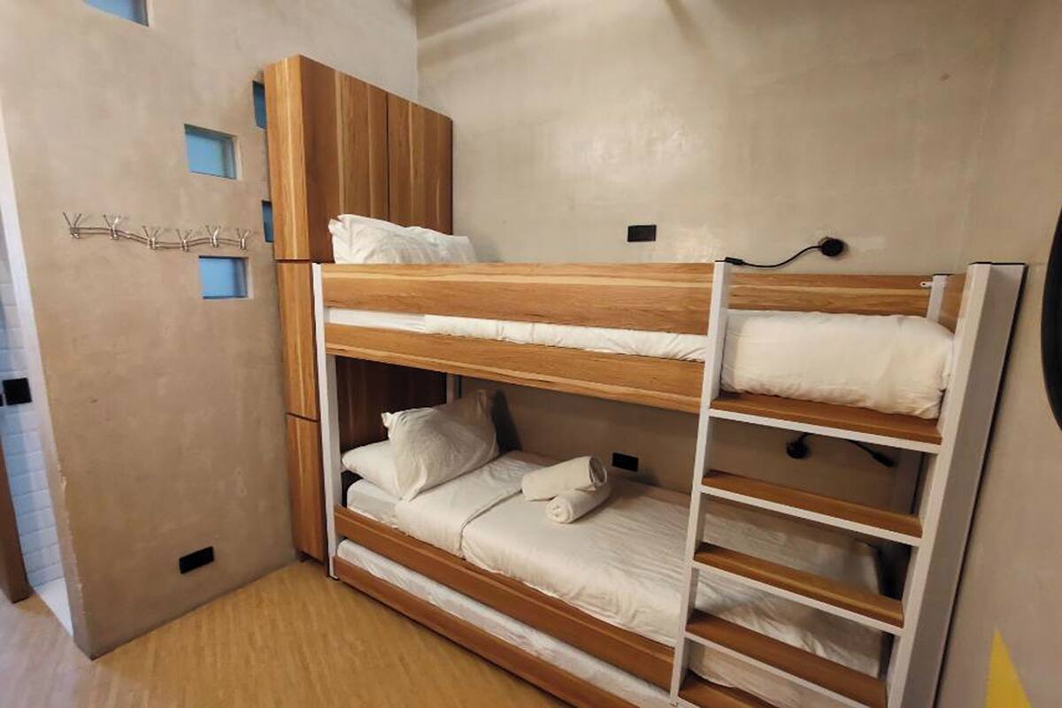 A bunk bed room with wooden headboard, white bedding, and a wall-mounted light fixture.