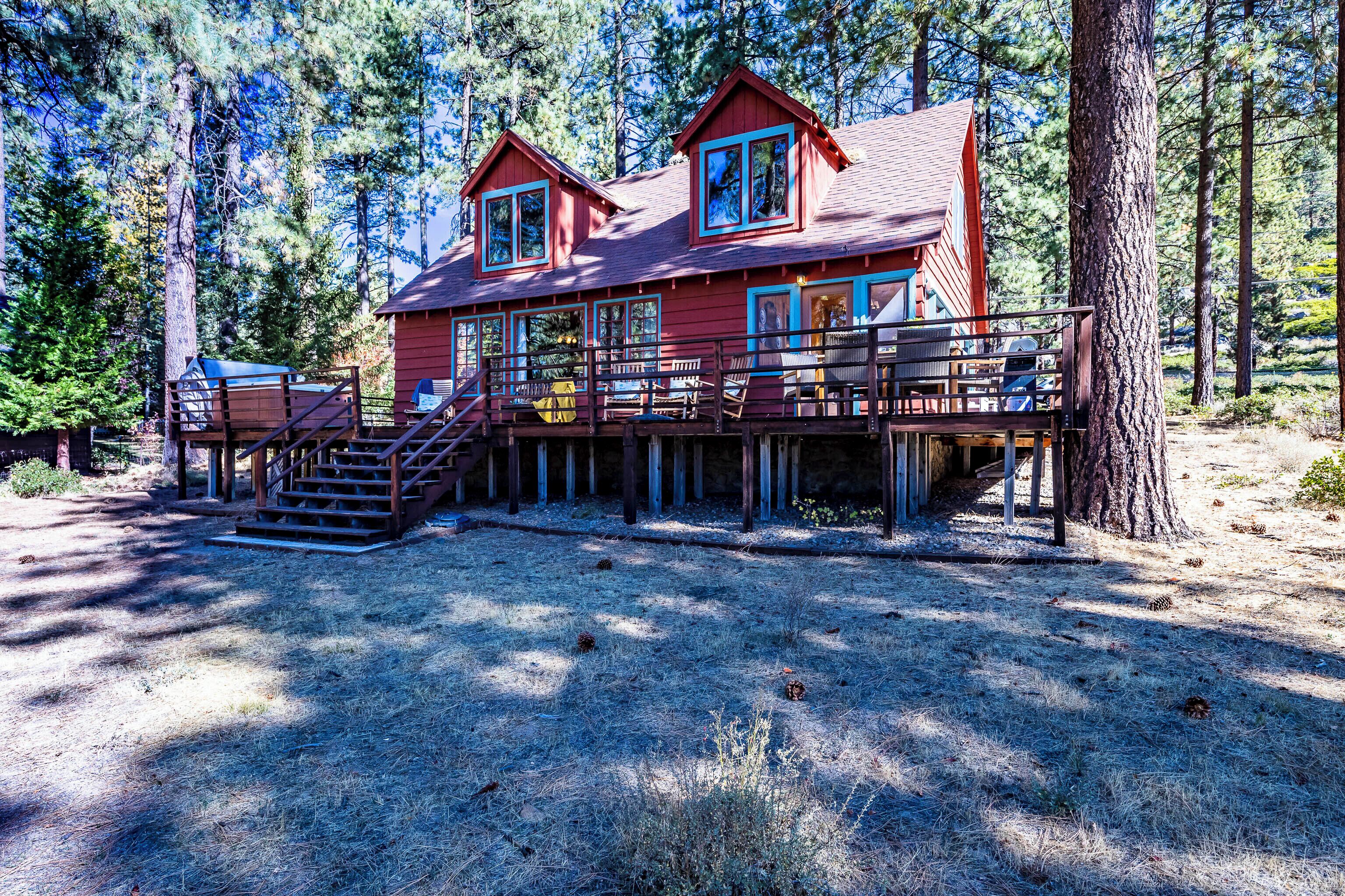 A two-story cabin with a deck, surrounded by trees.