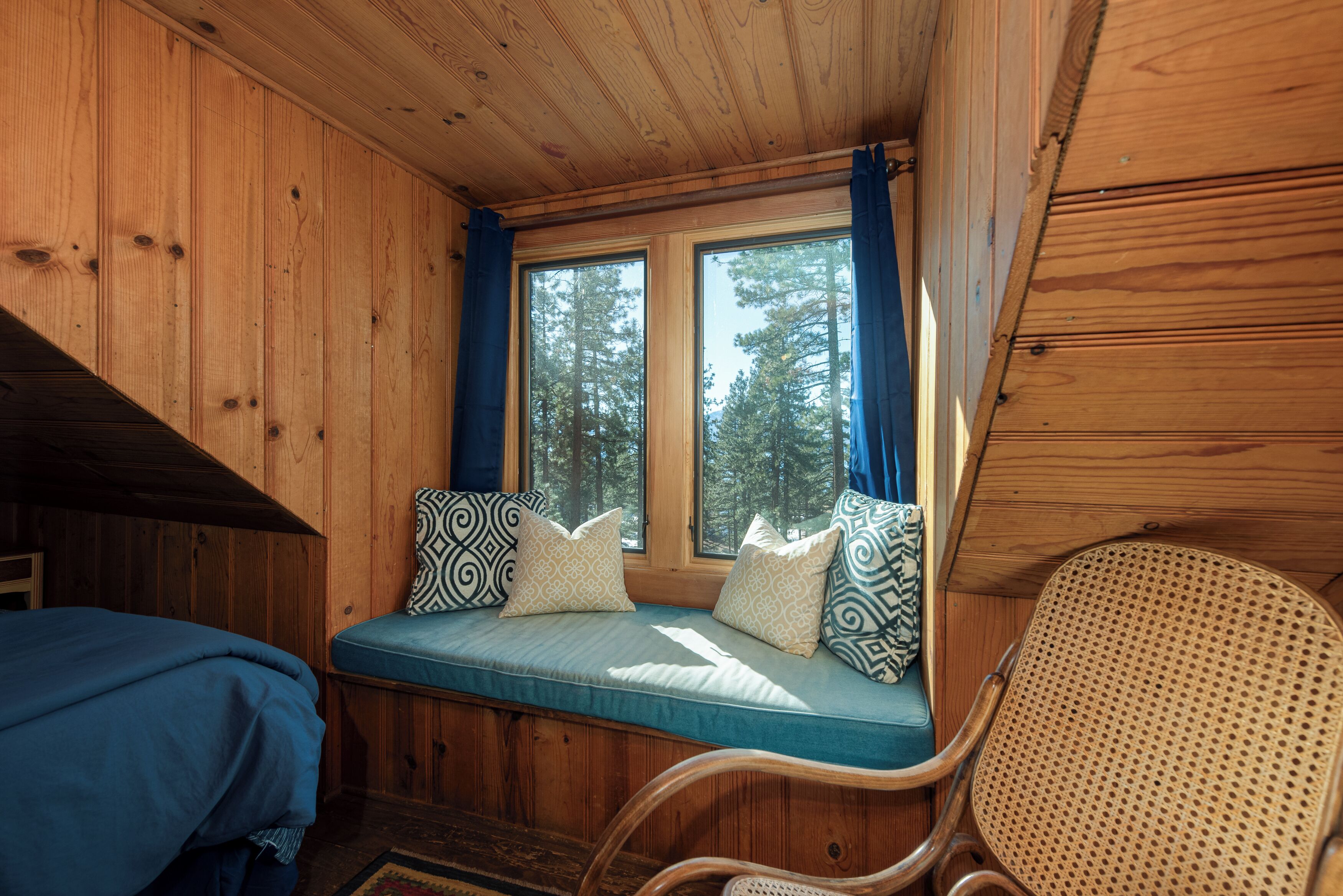 A cabin interior with a wooden interior, a bench with cushions, and a view of trees through a window.