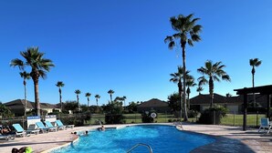 A swimming pool with a metal ladder, surrounded by palm trees and lounge chairs.