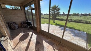A covered patio with large windows, a grill, and a patterned sofa.