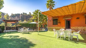 A patio with tables and chairs, a pool, and a building with a stone facade and a striped awning. - Beautiful home in Priego De Cordoba (Priego De Cordoba)