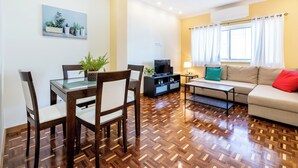 A modern living room with a dining area, wooden parquet flooring, a sofa, a TV, and a painting on the wall. - Urban City View Apartment (Lagos)