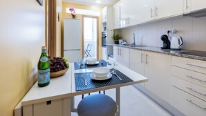 A modern kitchen with white cabinets, a dining table with a bowl of fruit, a bottle, and a coffee maker. - Urban City View Apartment (Lagos)