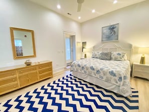 Un dormitorio con cama, cómoda, espejo, un cuadro y alfombra estampada.