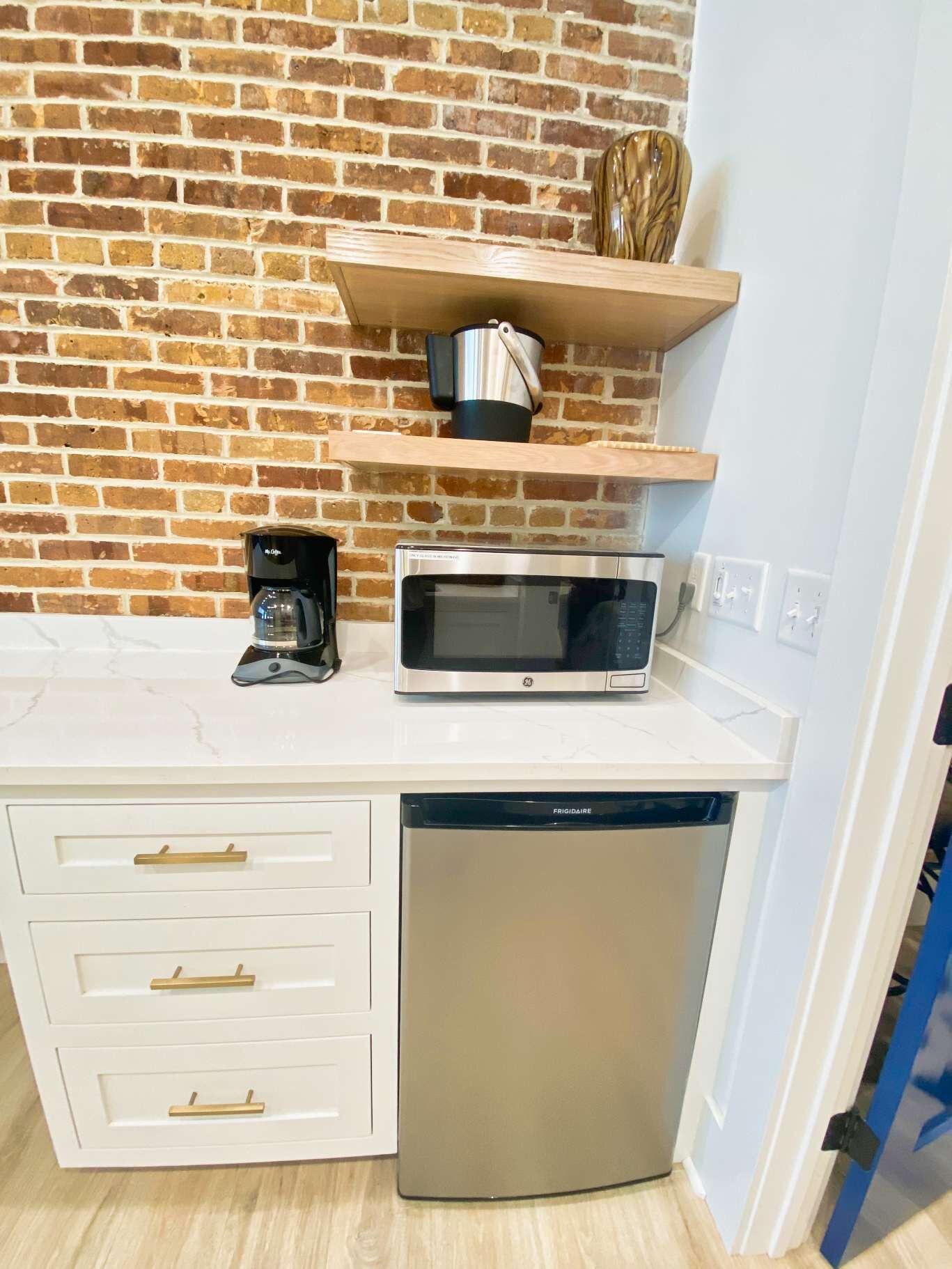 A kitchen with a brick wall, a microwave, a coffee maker, and a dishwasher.