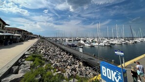 Un port de plaisance où sont amarrés de nombreux voiliers, une côte rocheuse et une promenade piétonne.