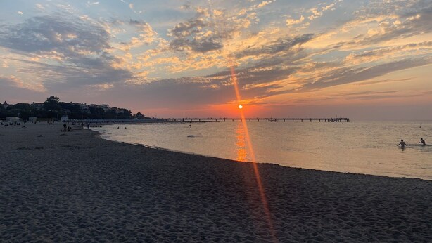 Une plage au coucher du soleil, avec une jetée qui s’avance dans l’eau.