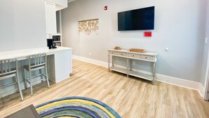 A modern kitchen with a white countertop, stainless steel appliances, and a dining area with metal chairs. - Crab Crib Loft in Historic Downtown Cape Charles (Cape Charles)