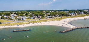 A coastal town with a sandy beach, a rocky breakwater, and residential houses in the background.