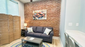 A living room with a brick wall, a sofa, a coffee table, and a colorful rug. - Crab Crib Loft in Historic Downtown Cape Charles (Cape Charles)
