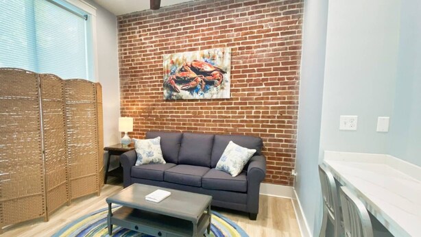 A living room with a brick wall, a sofa, a coffee table, and a colorful rug. - Crab Crib Loft in Historic Downtown Cape Charles (Cape Charles)