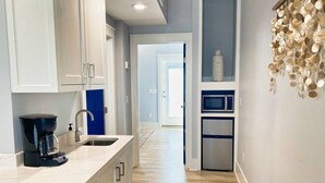 A modern kitchen with white cabinets, a coffee maker, a microwave, and a refrigerator. - Crab Crib Loft in Historic Downtown Cape Charles (Cape Charles)