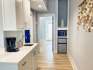 A modern kitchen with white cabinets, a coffee maker, a microwave, and a refrigerator. - Crab Crib Loft in Historic Downtown Cape Charles (Cape Charles)